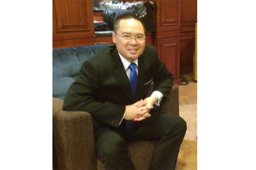 A man with glasses wearing formal suit is sitting on the sofa